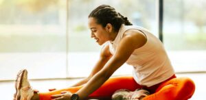 A woman in workout clothing sitting on the floor and stretching towards her foot