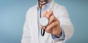 A doctor in a white coat holding out a stethoscope towards the camera