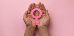 Two cupped hands holding a pink female gender symbol against a pink background, representing the practice's support for women's health and menopause care.