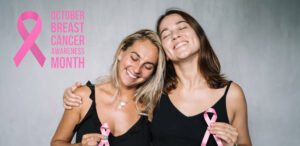 Two women embracing and holding pink ribbons, beside a pink ribbon graphic and the words "October — Breast Cancer Awareness Month."